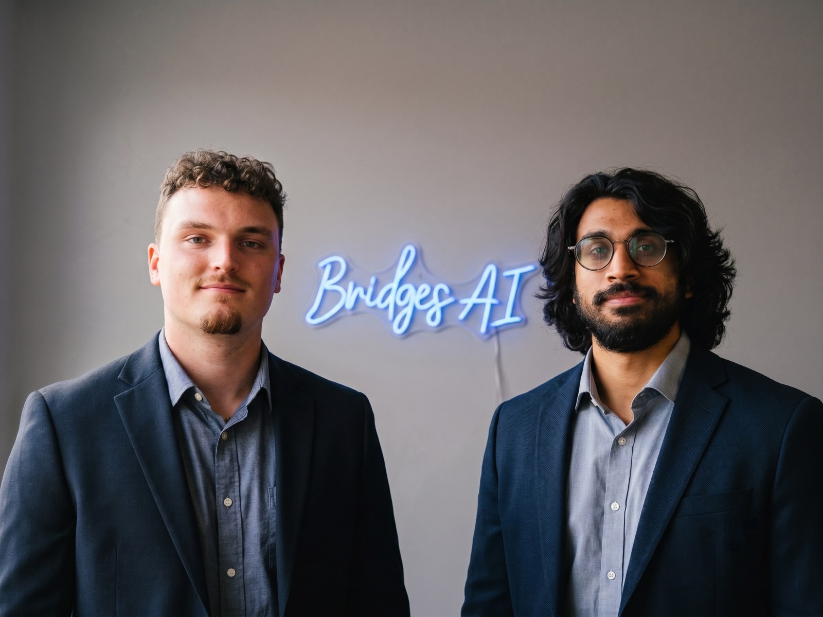 Benjamin Olmsted and Nevyn Duarte, founders of Bridges AI Consulting, beside the Bridges AI neon sign in their New Jersey office